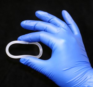 Vaginal ring held up for display in gloved right hand.